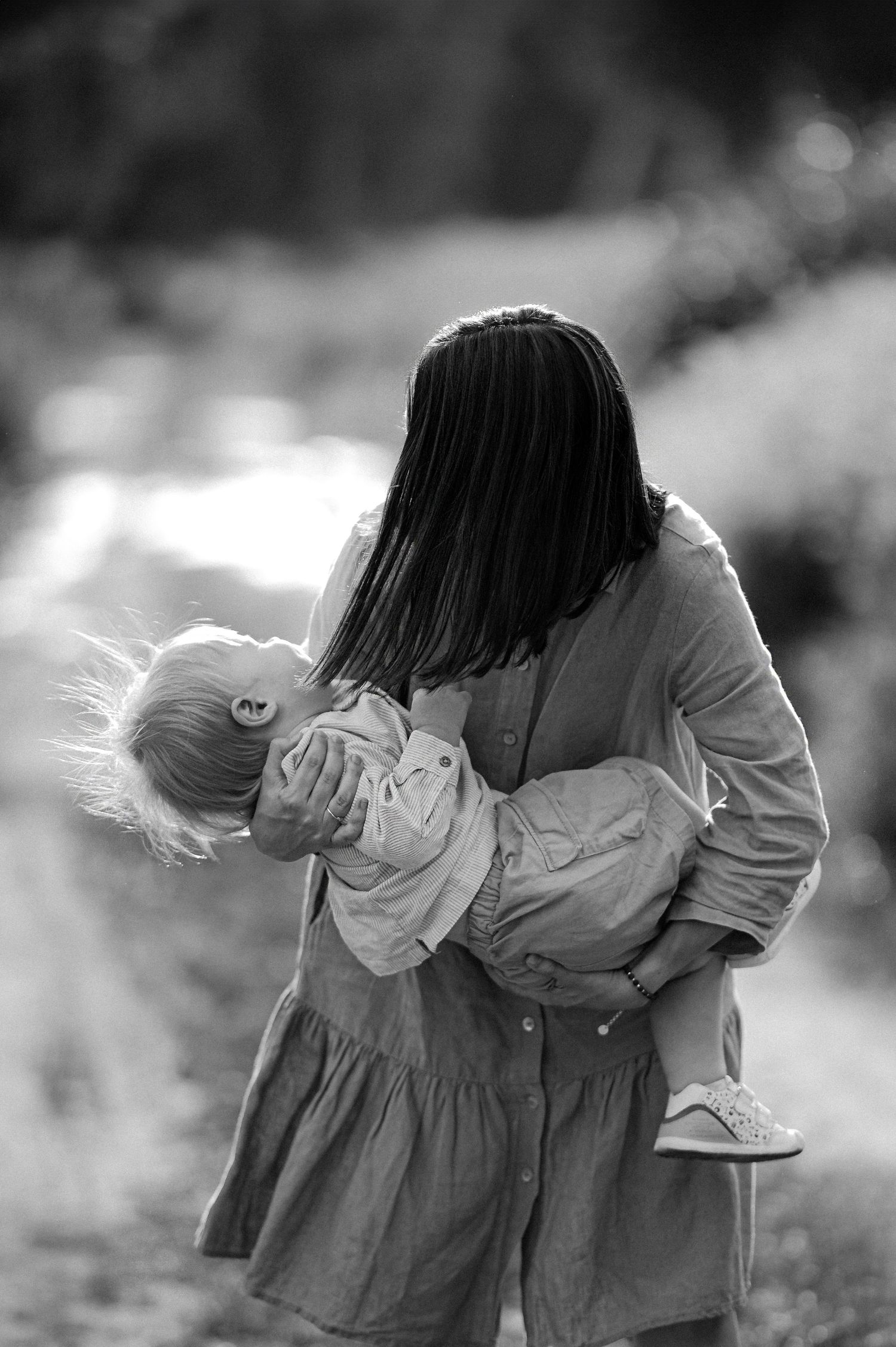 Black and white photo of a mother tenderly holding her young blonde child outdoors.