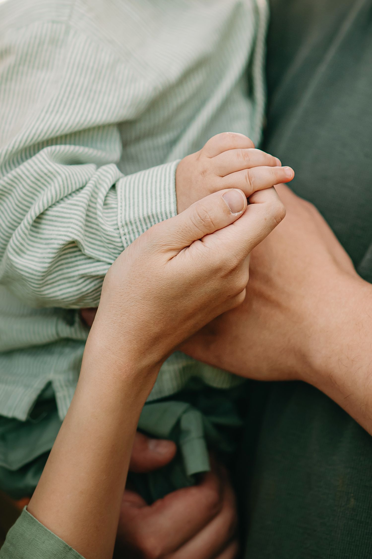 Close-up of two people gently holding hands, wearing green clothing, symbolizing love and connection.