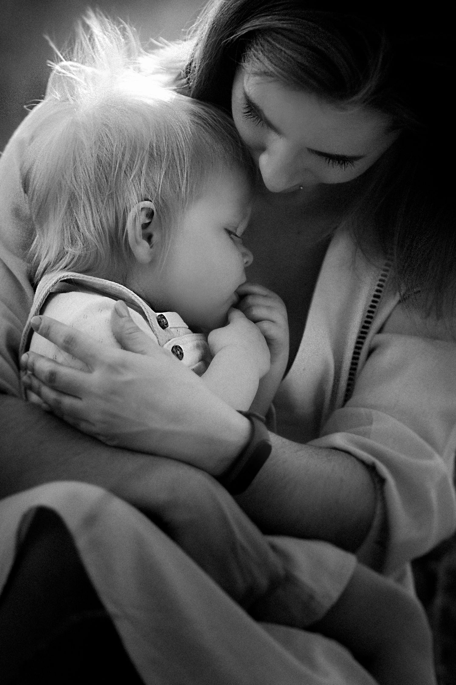 Black and white photo of a mother tenderly holding and breastfeeding her infant child in a warm embrace.
