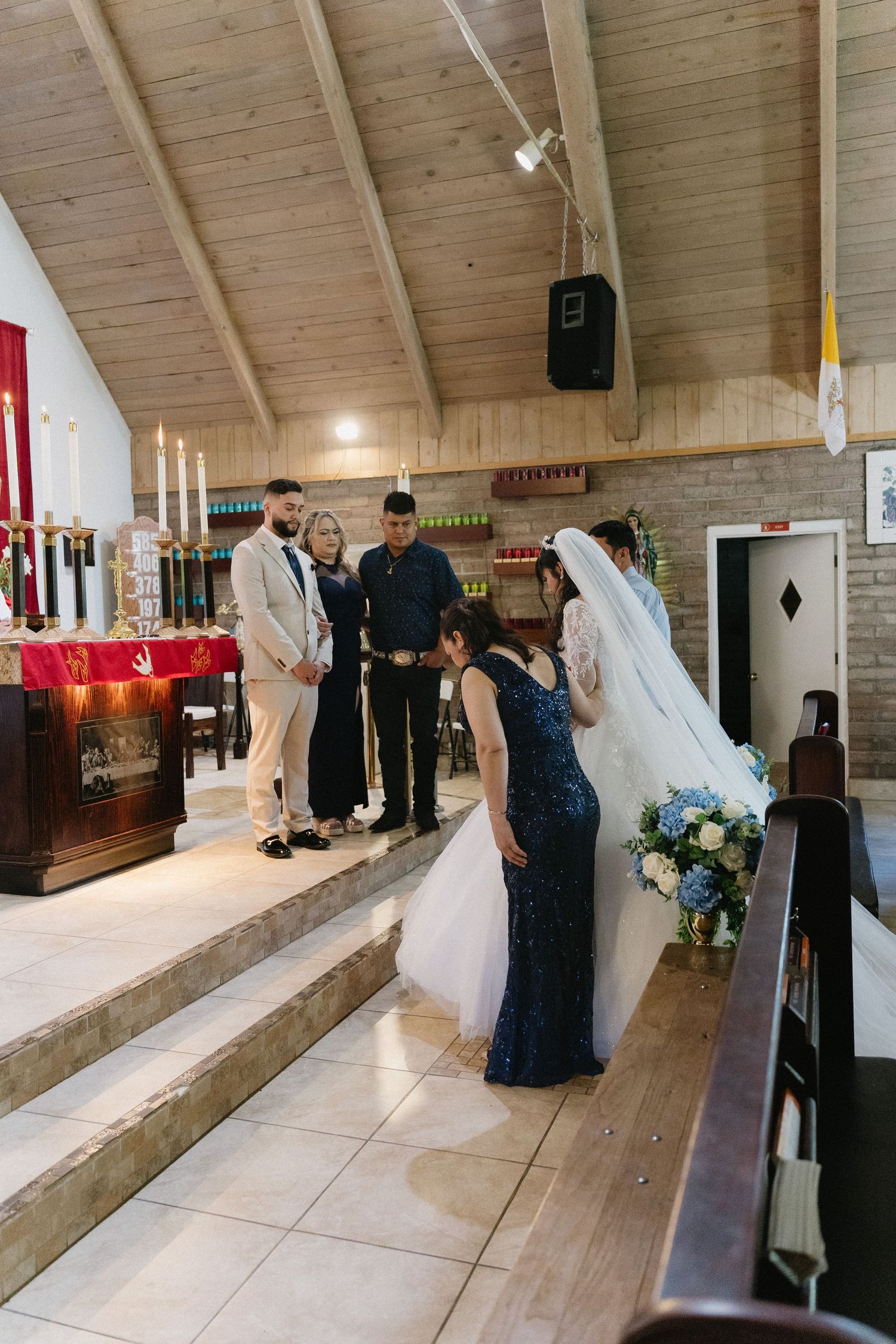 Bride and groom at church altar during wedding ceremony with bridesmaid holding bouquet of blue and white flowers.