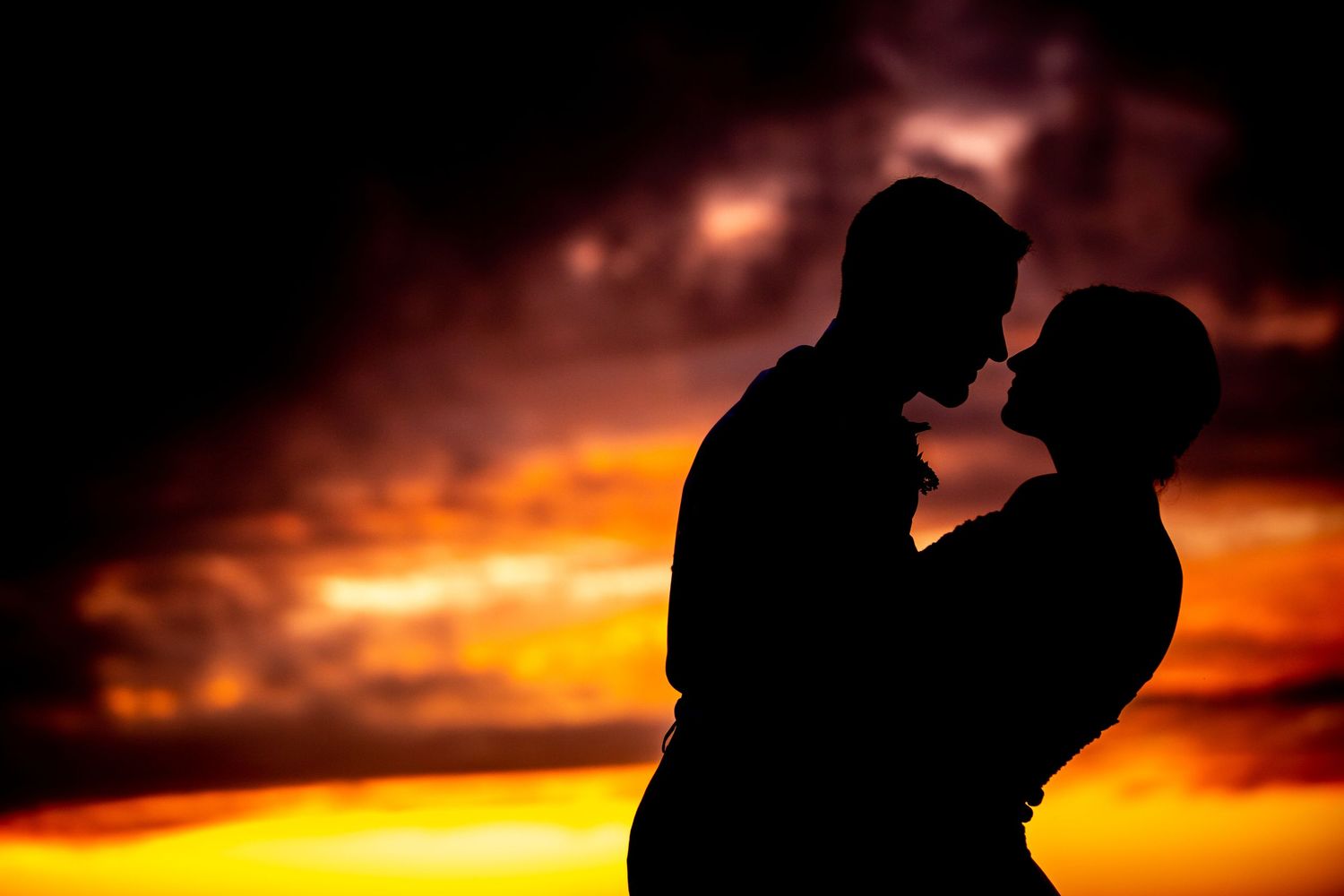 Romantic couple silhouette embracing against a dramatic fiery orange and red sunset sky.