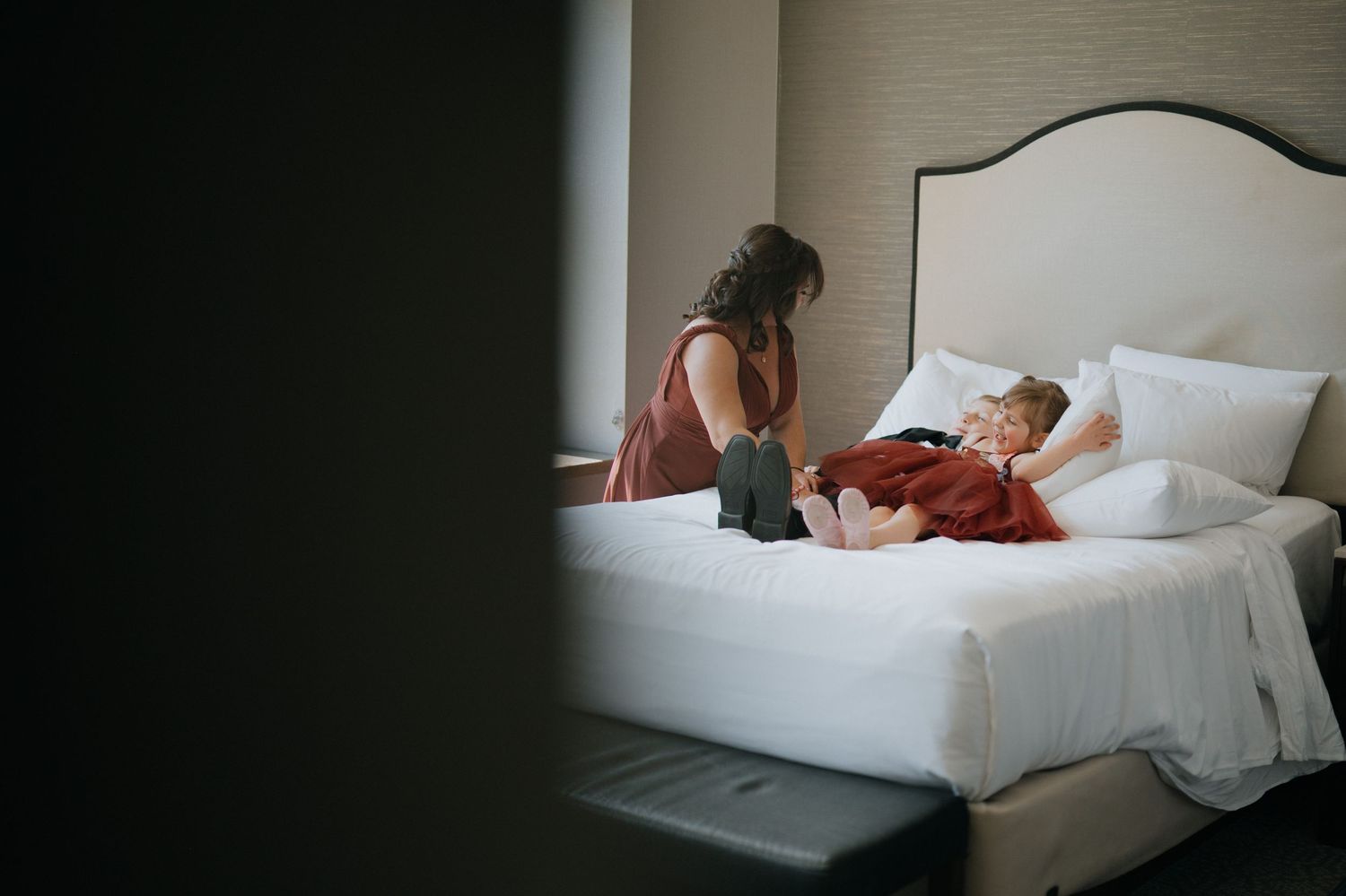 Mother sitting on hotel bed with child lying down in a warm, intimate candid moment.