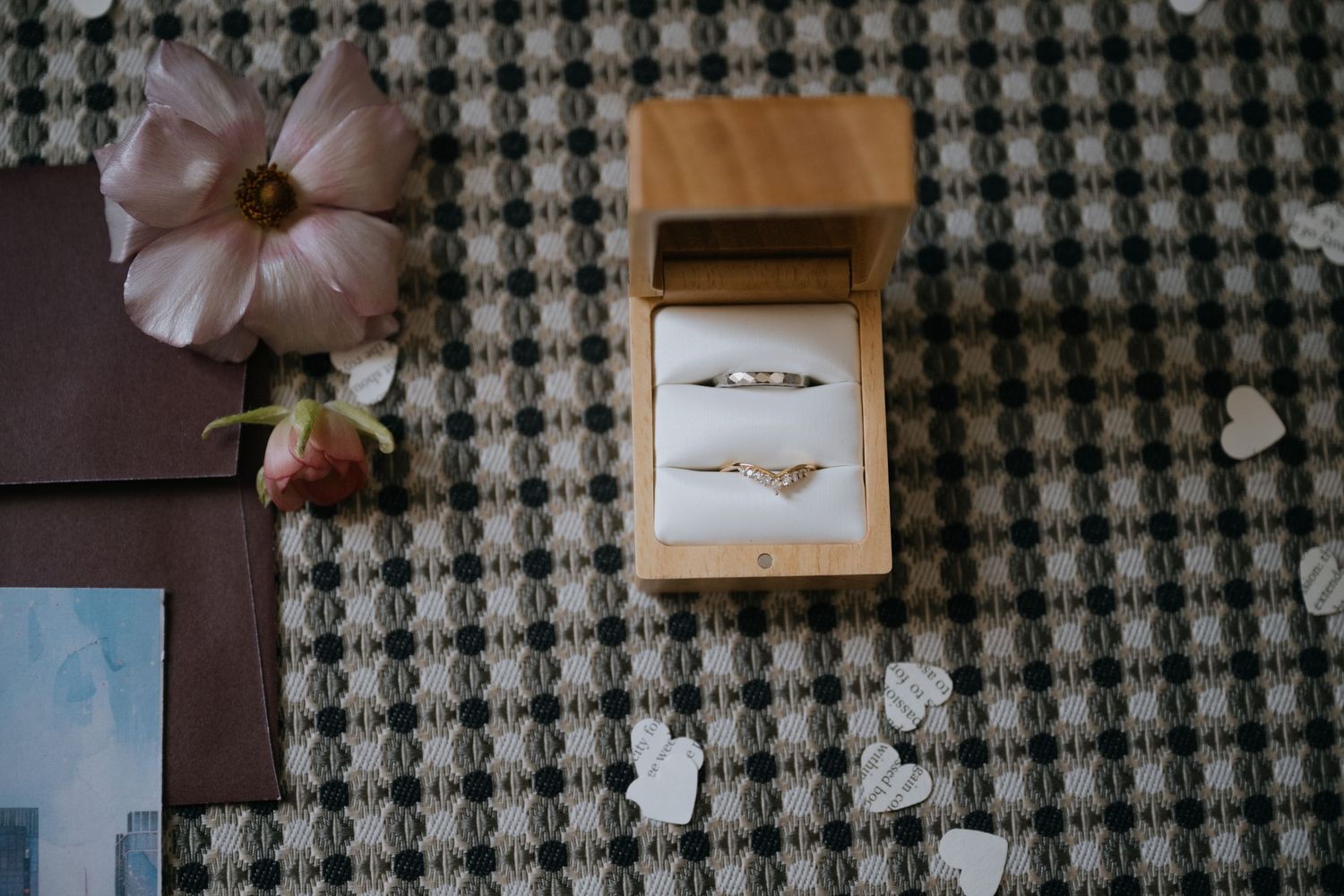 Two elegant gold wedding rings displayed in a wooden ring box surrounded by flowers and petals.