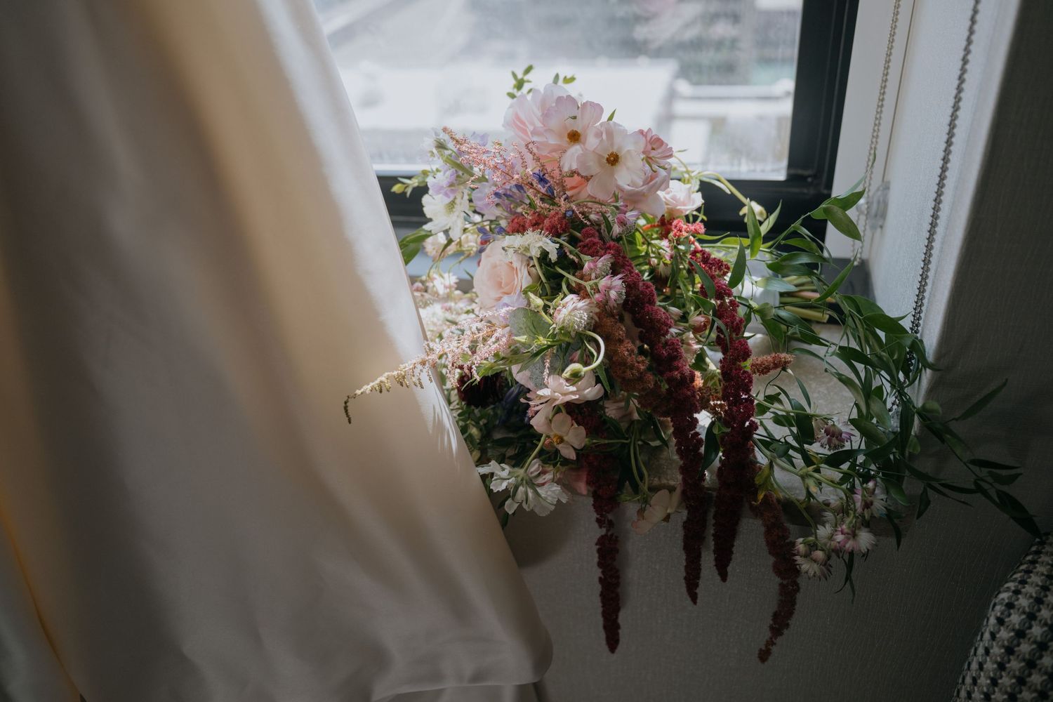 Cascading bridal bouquet with pink and burgundy blooms rests on a windowsill.
