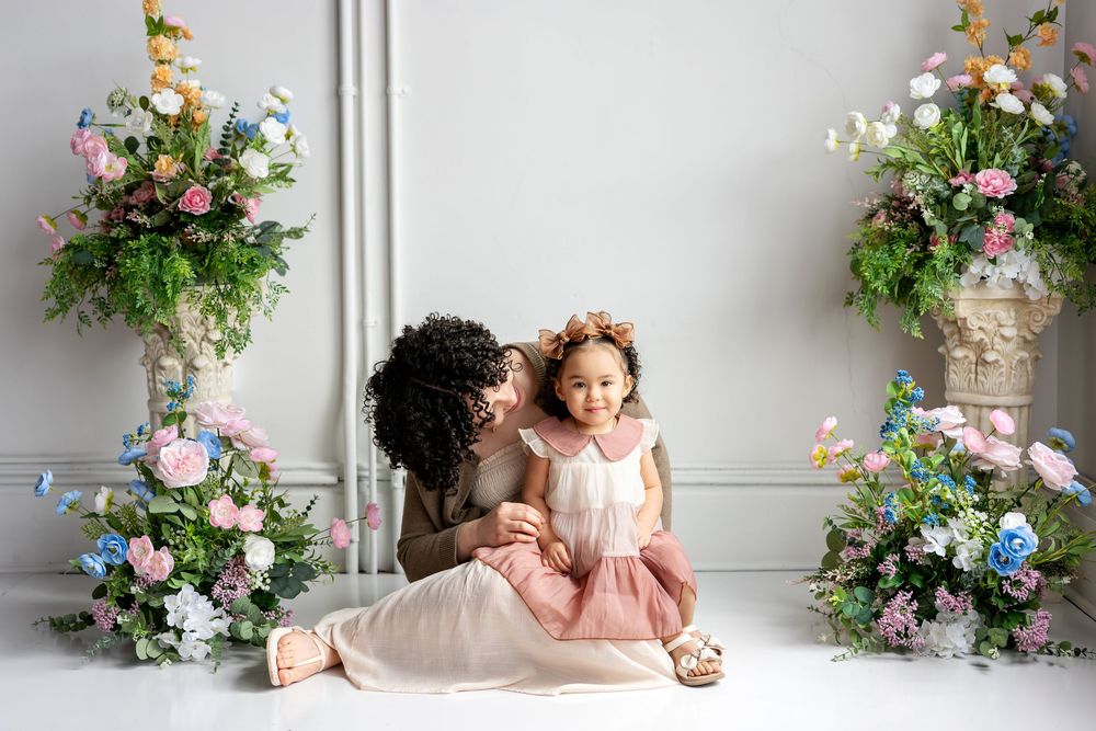 Mother and toddler daughter share a tender moment surrounded by colorful floral arrangements.