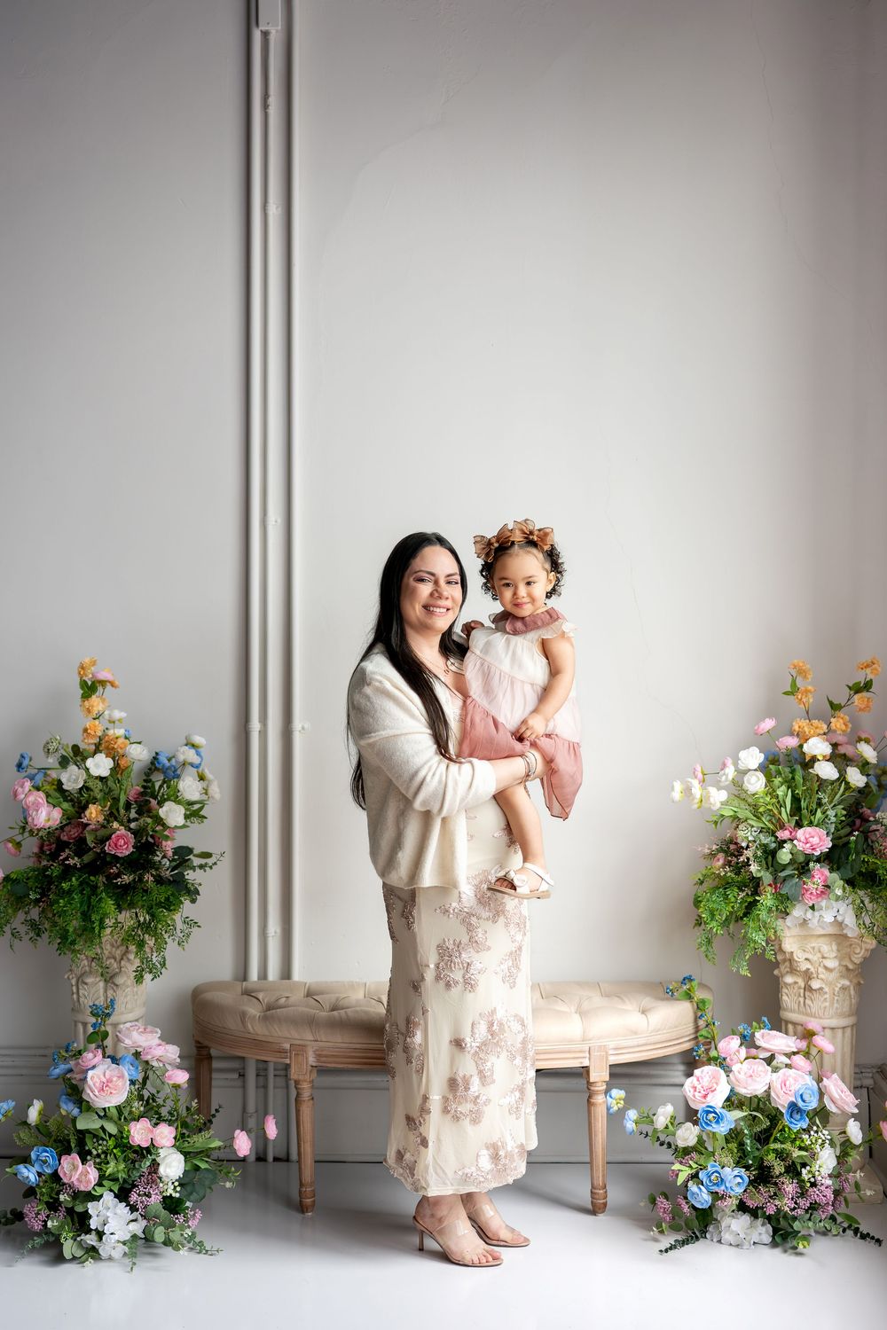 Smiling woman holds her young daughter in a floral spring studio portrait setting.