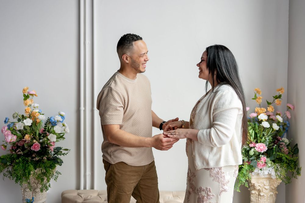 Smiling couple holding hands facing each other in a bright studio with colorful floral decor.