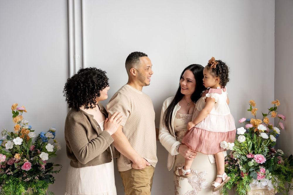 A family of four shares a candid moment surrounded by pastel spring floral arrangements in a bright white studio.