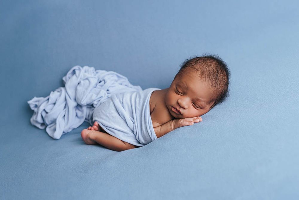 Sleeping newborn baby wrapped in light blue cloth on blue background.