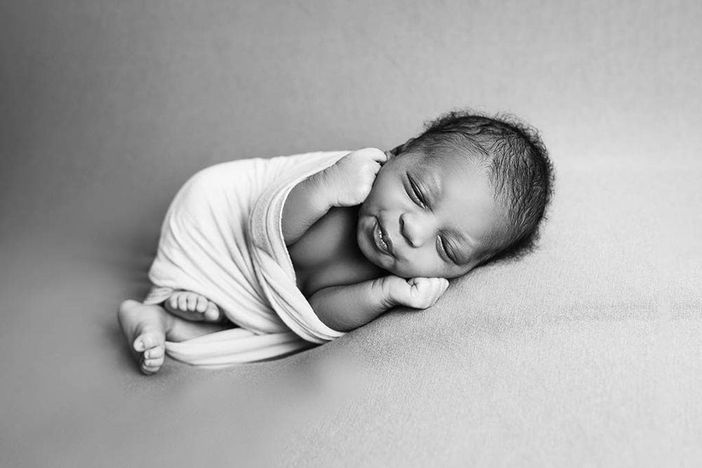 Sleeping newborn baby wrapped in white swaddle cloth, black and white photography.
