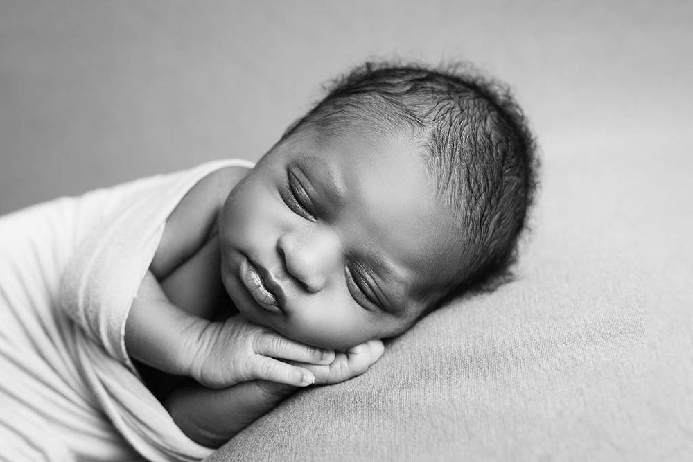 Peaceful sleeping newborn baby wrapped in white swaddle, black and white portrait photography.