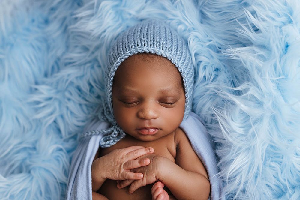 Sleeping newborn baby in blue knit bonnet wrapped in soft blue fur blanket, peaceful infant portrait photography.