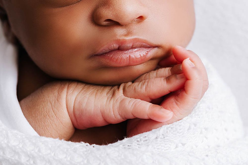 Close-up of a sleeping newborn baby's lips and tiny hand wrapped in a soft white blanket.