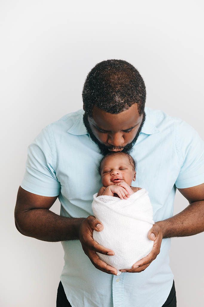 Dad holding newborn baby boy against white backdrop.