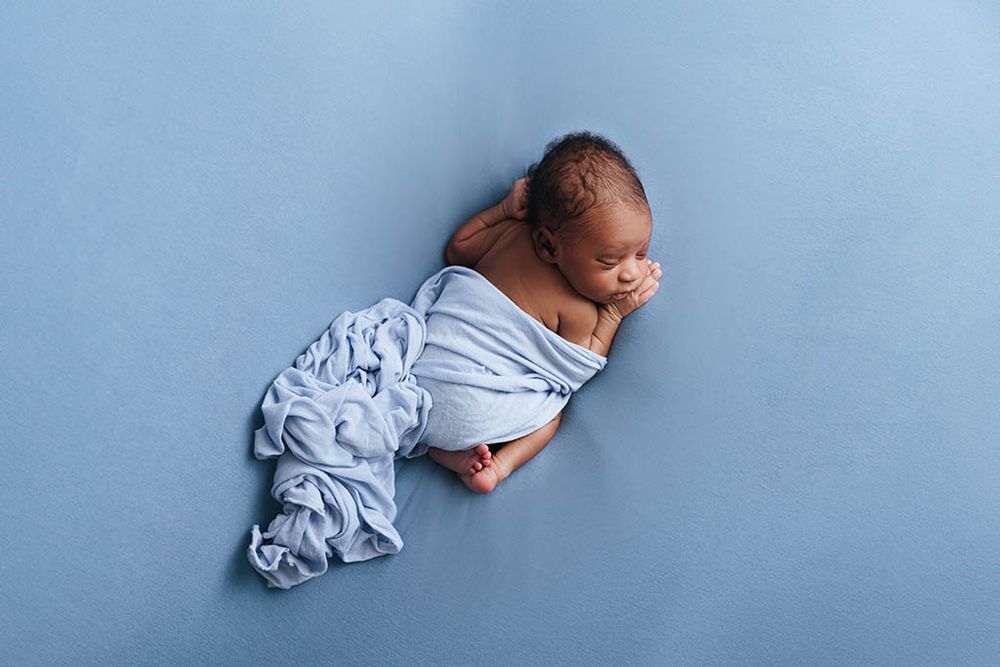 Newborn baby wrapped in light blue cloth sleeping peacefully on a blue background.