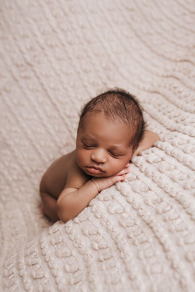 A peaceful newborn baby sleeps curled up on a soft cream textured blanket.