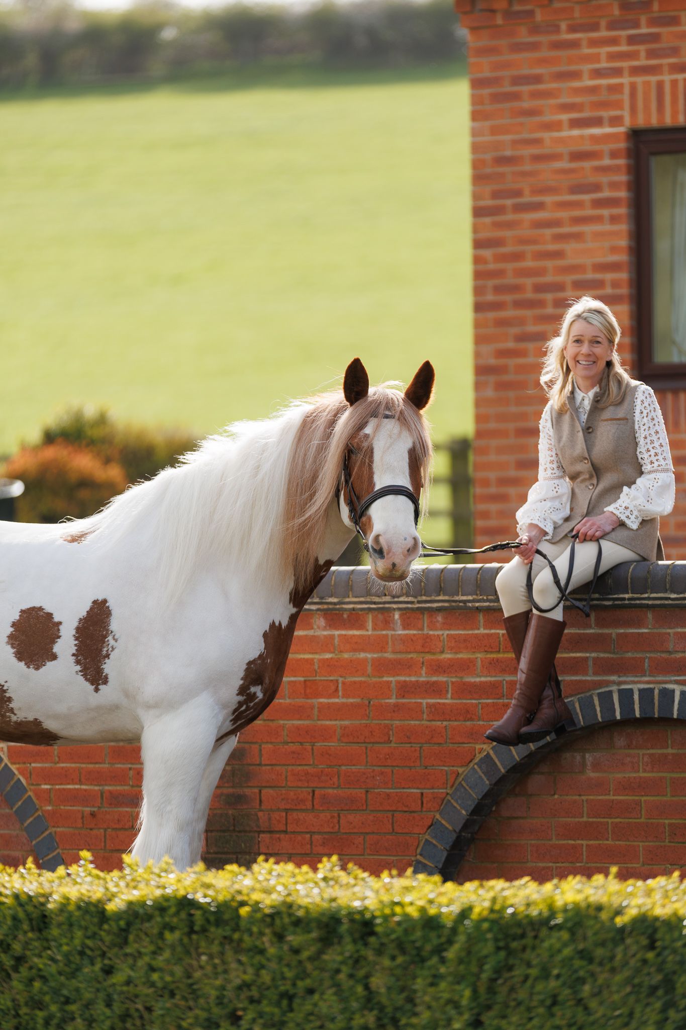 A brown horse and rider in a white sweater pose together against autumn foliage in soft natural lighting.
