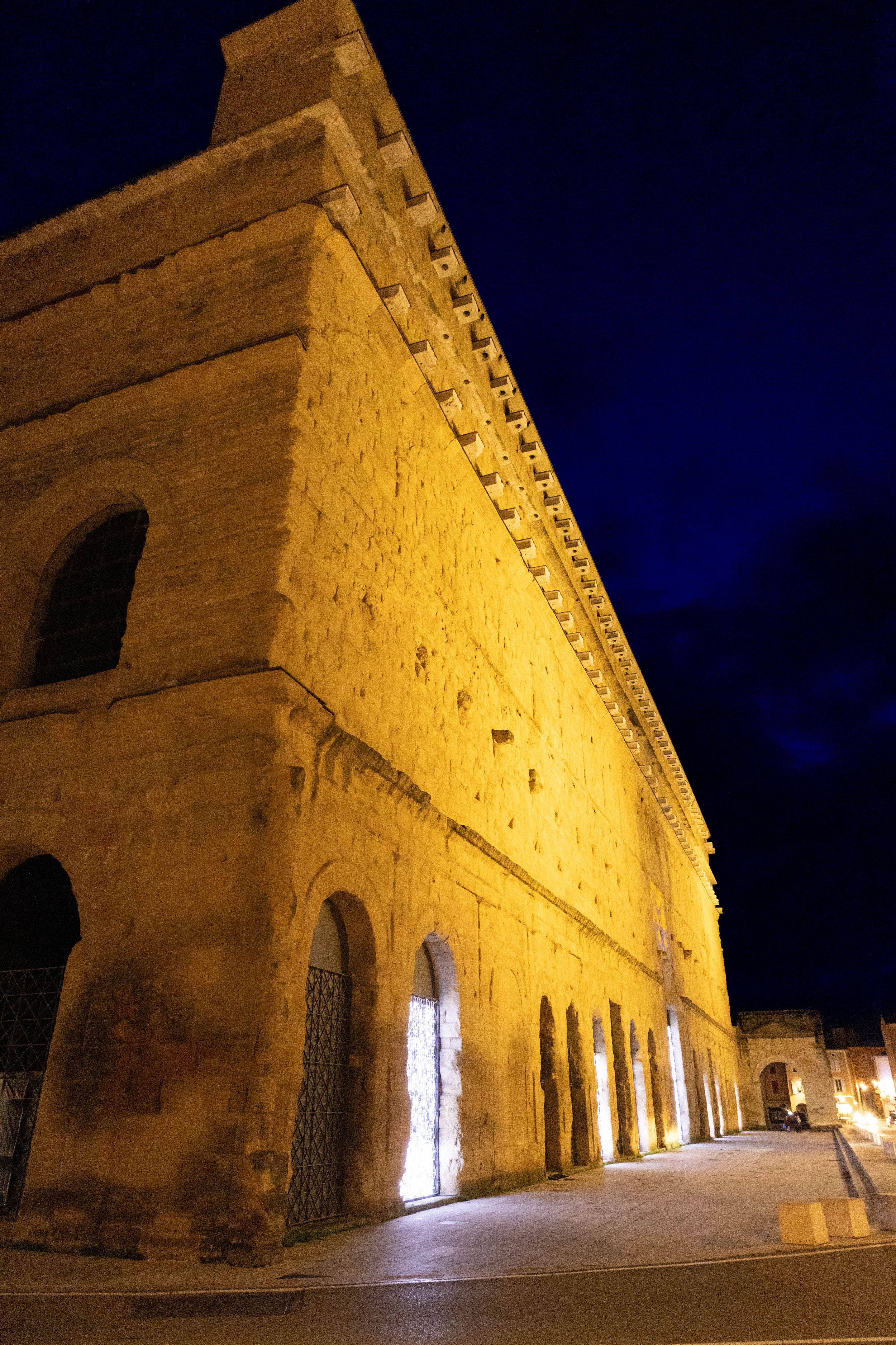 Ancient stone building illuminated at night with warm golden lights against a deep blue sky.