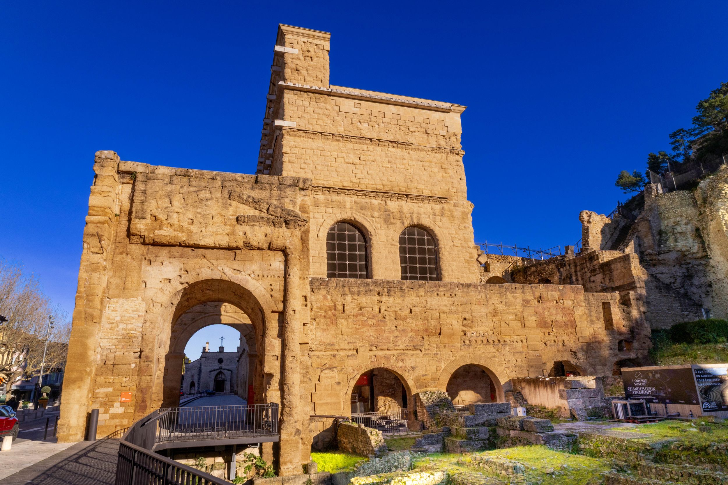 Ancient stone ruins with arched gateway under vivid blue sky, showcasing medieval architecture in warm golden sunlight.