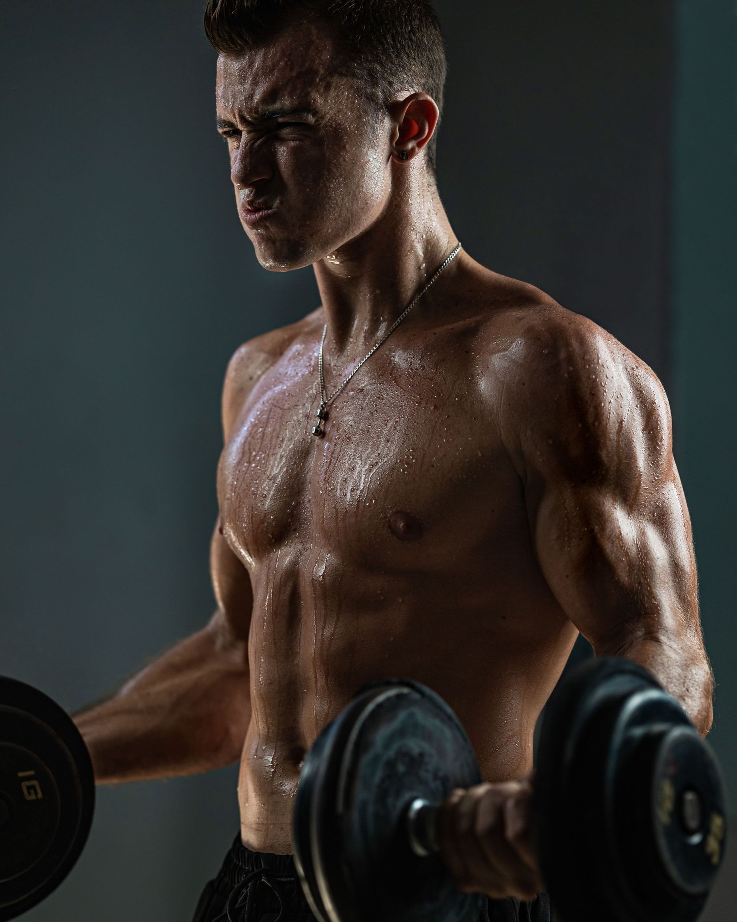 Athletic figure performing bicep curl with dumbbell in dramatic lighting showing muscular definition.