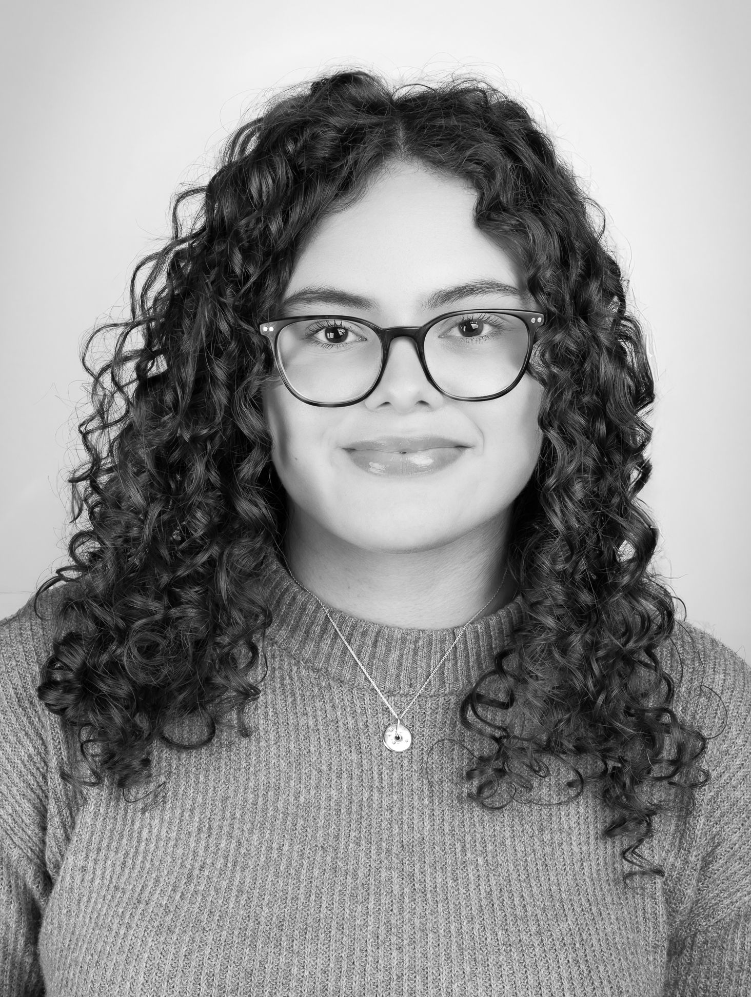 Black and white image of a girl with glasses smiling at the camera, front shot