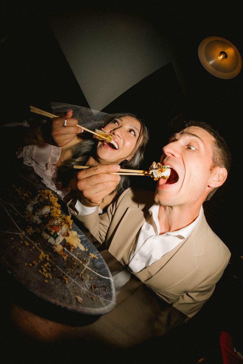 Couple sharing Asian food with chopsticks, laughing and eating together at a candlelit restaurant.