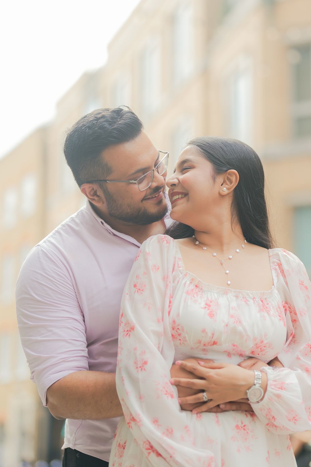A couple sharing a romantic moment outdoors, the man in a pink shirt embracing a woman in a floral dress.