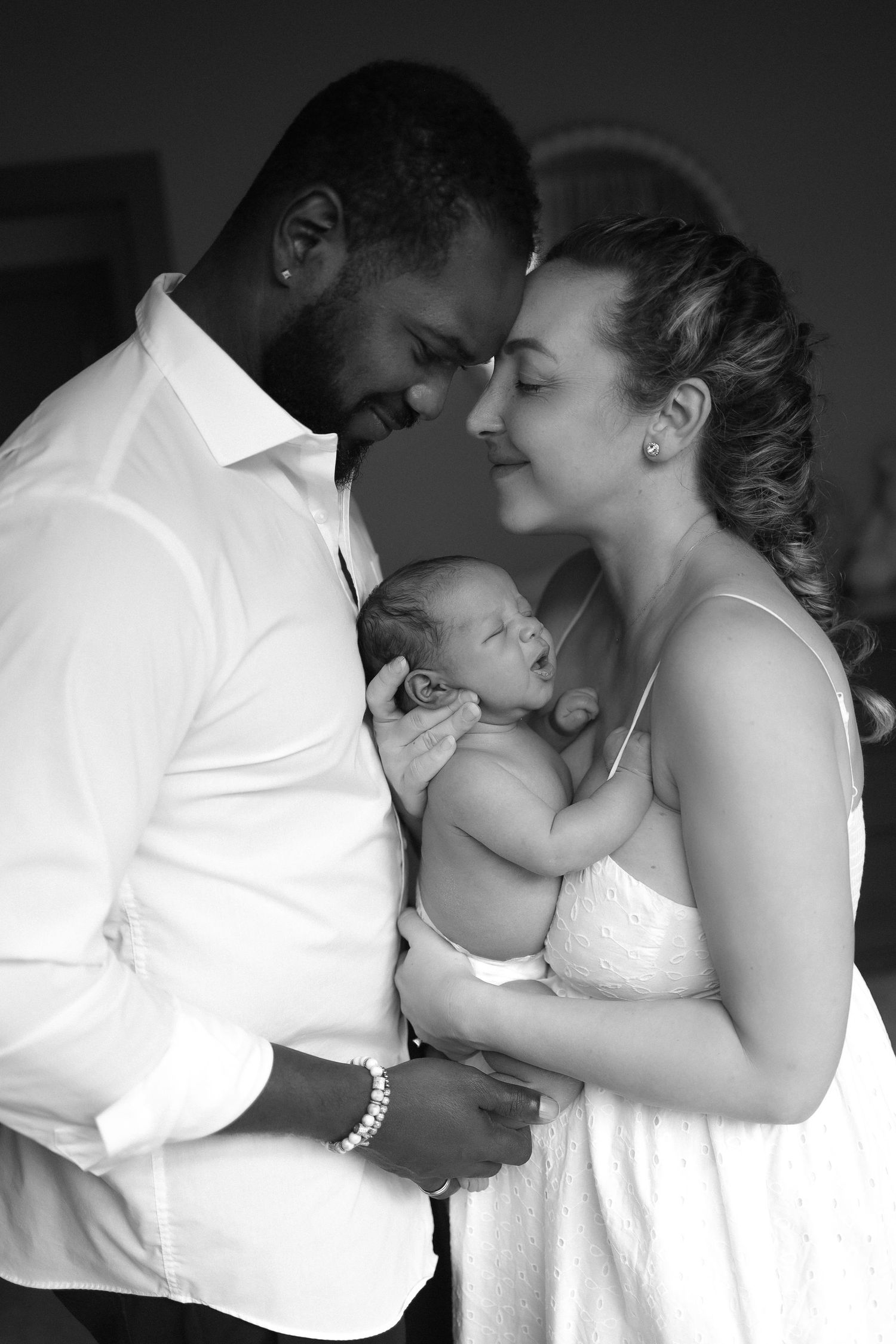 Intimate black and white portrait of new parents cradling their newborn baby.