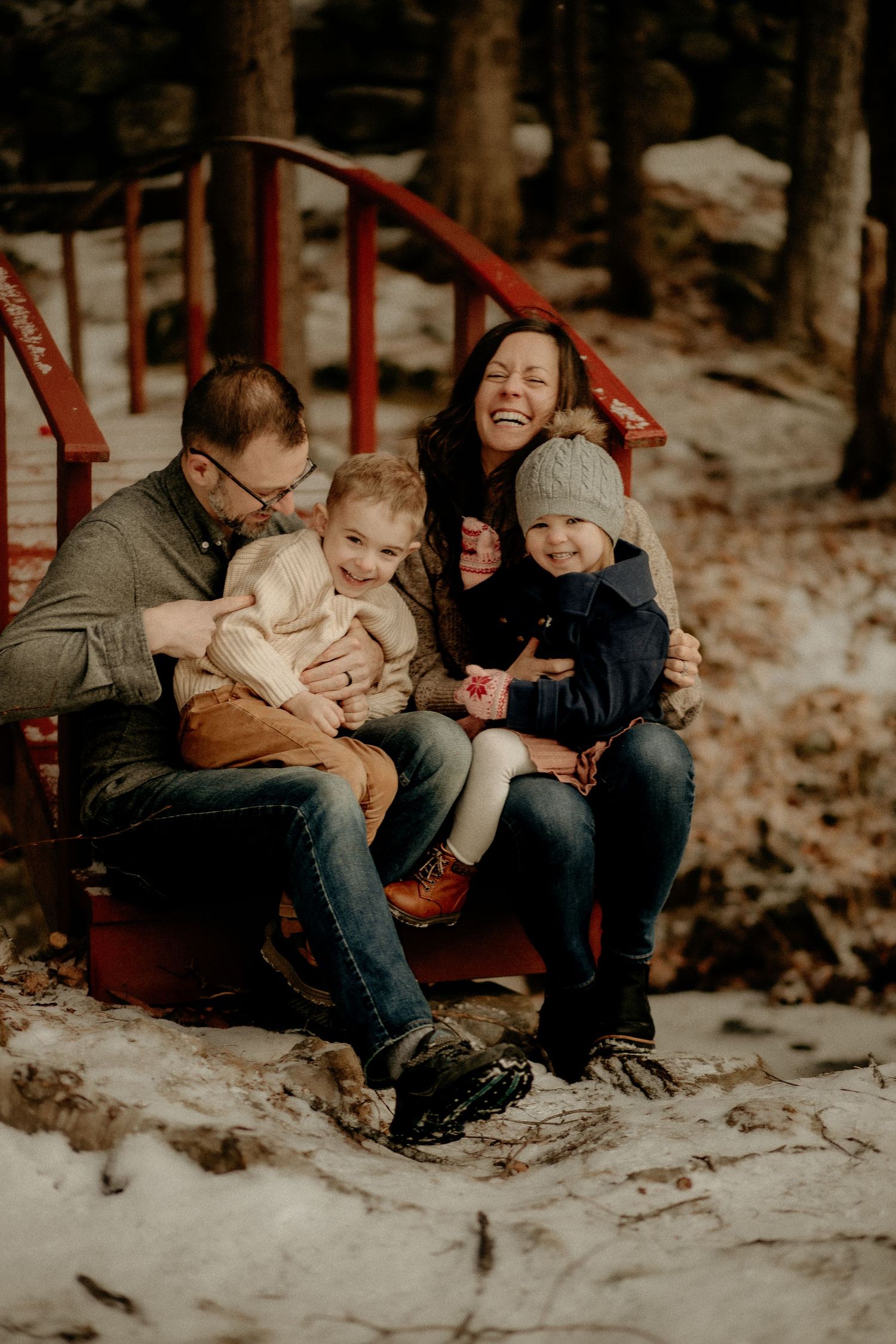 Family sitting together on red playground equipment during winter in a forest setting.