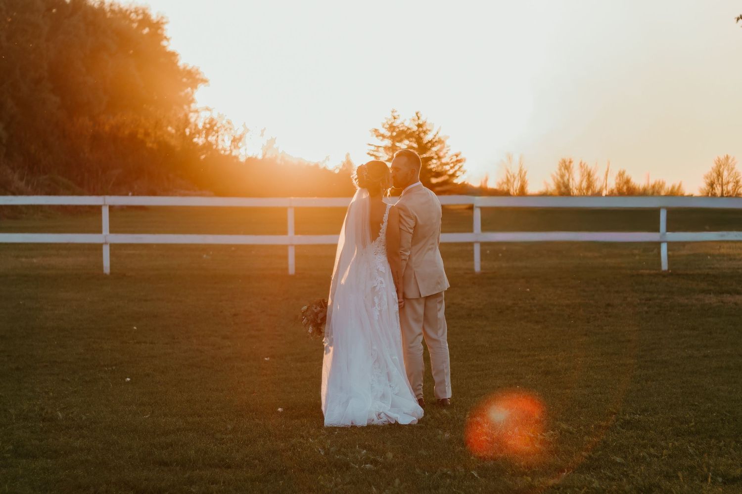 Figure draped in white sheet sits in golden sunlit field at sunset.