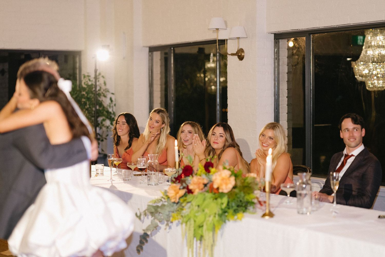 Wedding reception table decorated with greenery and candlelight as guests celebrate the newlyweds.
