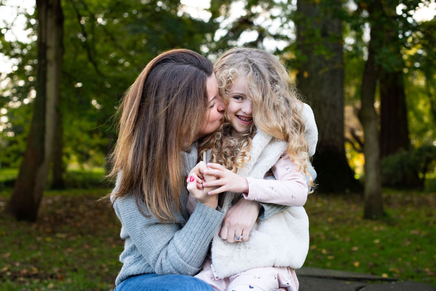 Mum kissing her 5 year old daughter on the cheek, whilst she looks cheekily at the camera during an Autumn photoshoot