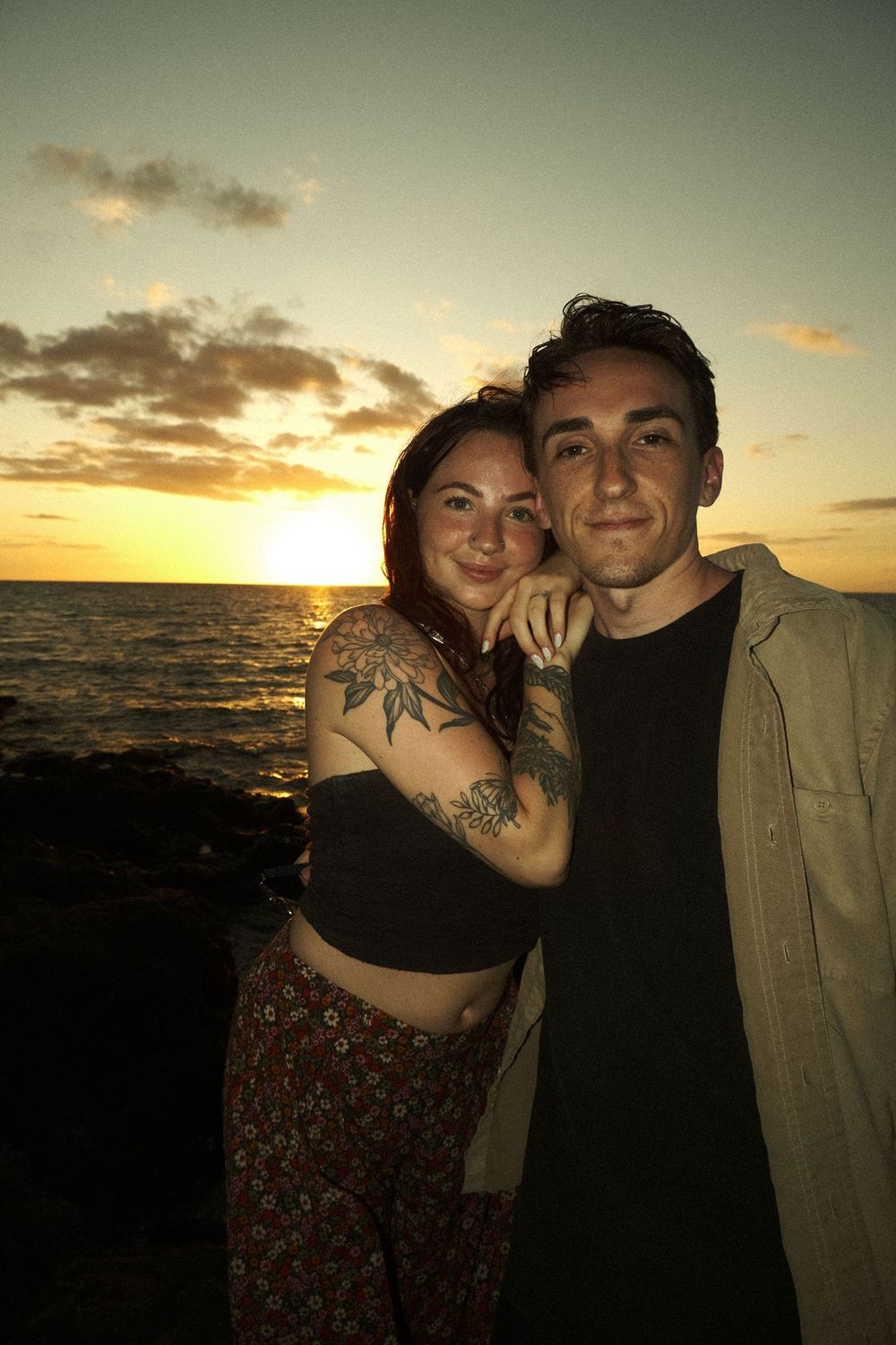 A couple poses together against a beautiful ocean sunset backdrop, creating silhouettes on the beach.