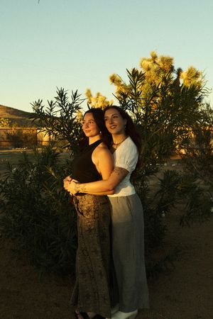 Two people embrace in a warm sunset glow among desert plants and yellow wildflowers.