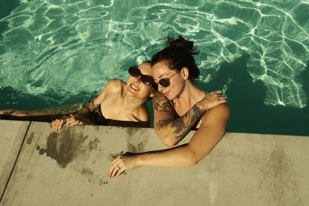 People swimming in crystal clear turquoise water and lounging at the edge of a pool on a sunny day.