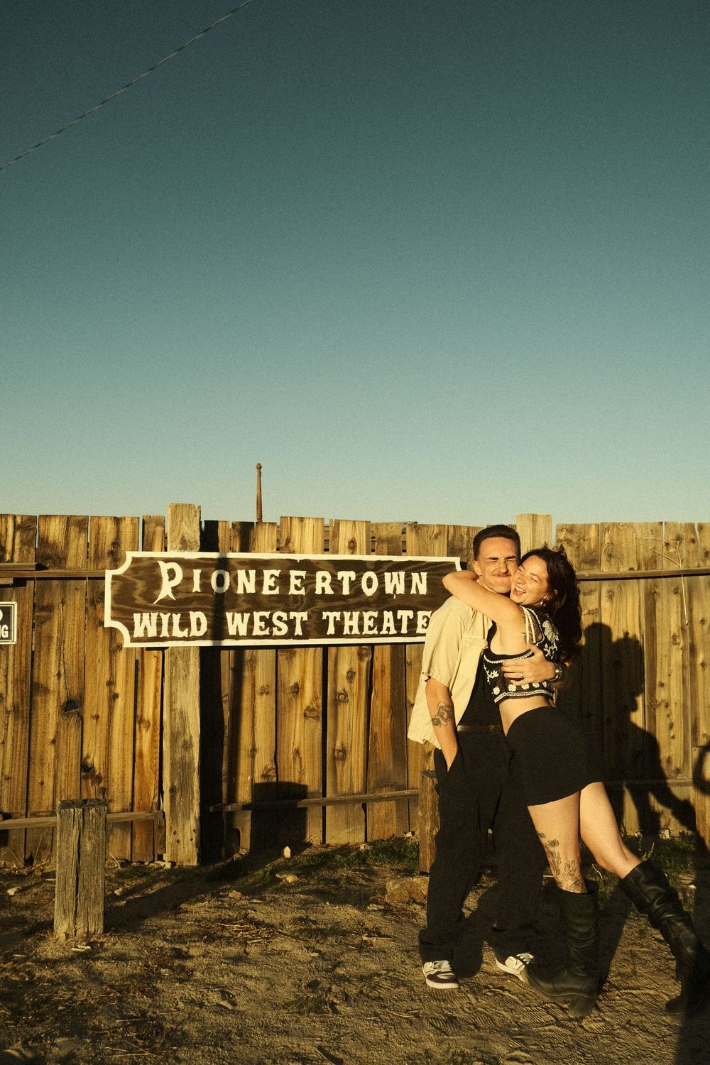 A series of panoramic shots showing a rustic wooden fence with signs for 'Wild West Theatre' and 'Pioneertown' at sunset.