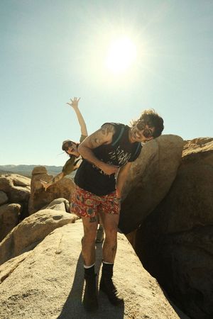 A person performs a yoga pose on a rocky cliff edge against a bright sunlit sky.