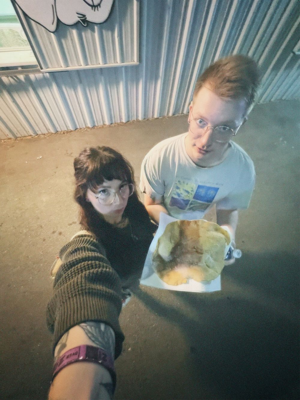 Two people taking a selfie while inside an industrial space with corrugated metal walls.