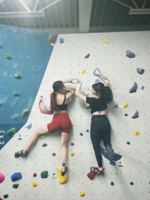 Two climbers scale a white indoor climbing wall with colorful holds at a bouldering gym.