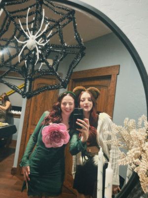 Mirror selfie showing Halloween costumes with a large decorative spider and black sparkly web in the corner.