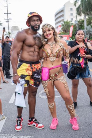 Two carnival revelers pose in festive costumes at Cayman Islands Carnival 2024, featuring elaborate gold beadwork and colorful swimwear.