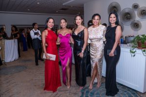 Five elegantly dressed women posing together at a formal gala event in evening gowns.