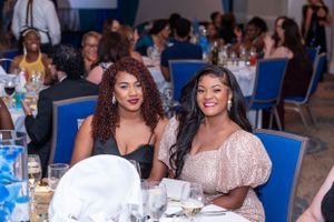 Two women smiling at a formal banquet event, seated at a decorated table in an elegant venue.