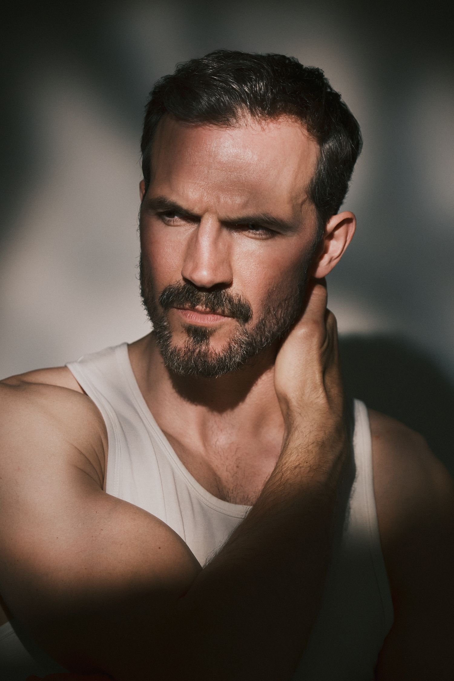 Bearded man in dramatic soft lighting, creating shadows across his face, giving a contemplative look