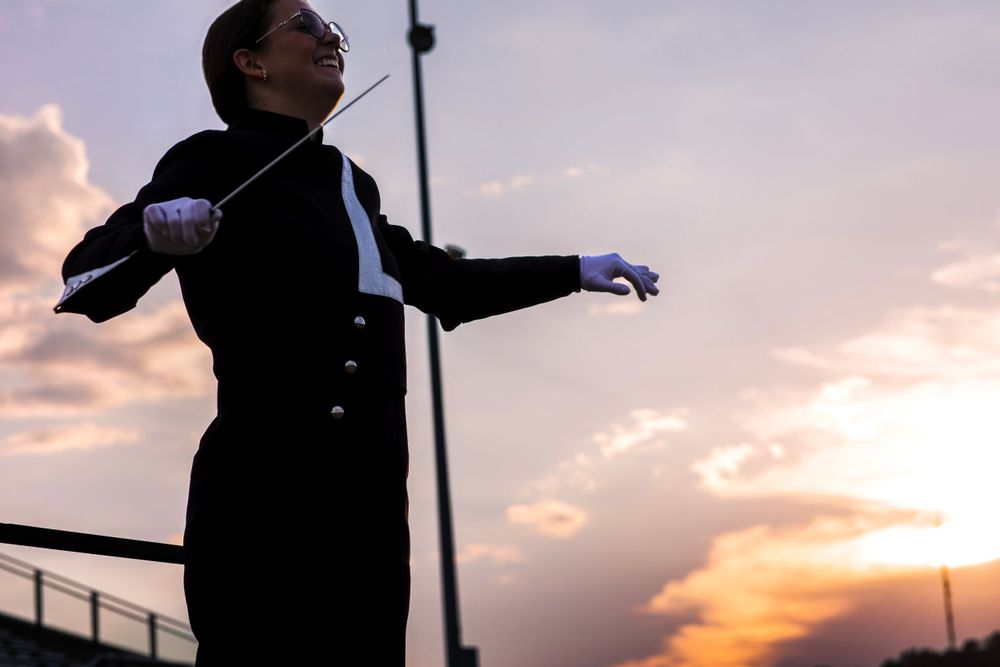 Dramatic silhouette of a conductor with arms outstretched against an orange sky.