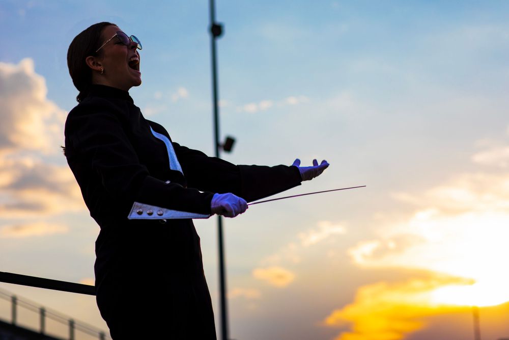 A conductor in formal attire leads with dramatic gestures during sunset.