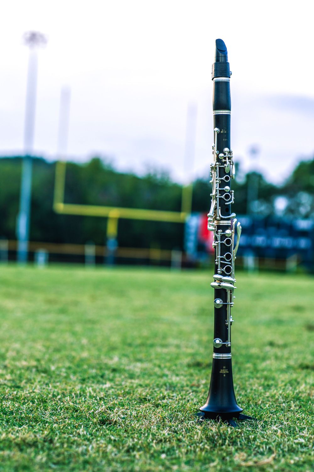 A clarinet stands upright on a grassy field with football goalposts in the background.