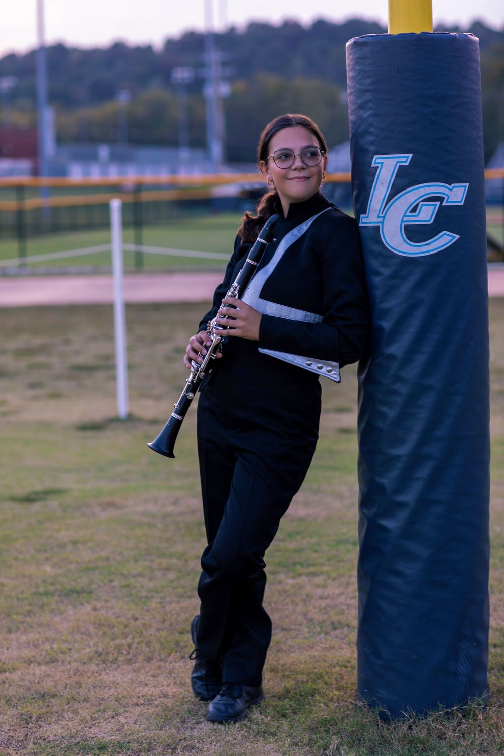 Band performer with clarinet poses next to LC branded field post during sunset.