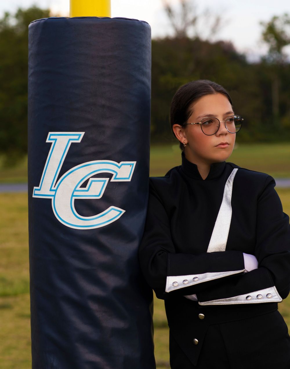 Marching band performer in black uniform stands beside blue LC branded field post.