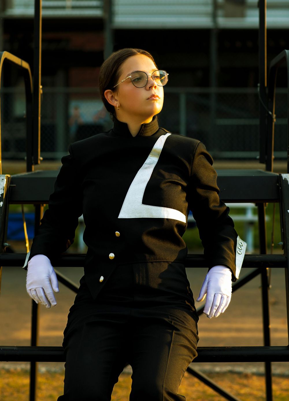 Marching band performer in black and white uniform strikes dramatic pose on bleachers.
